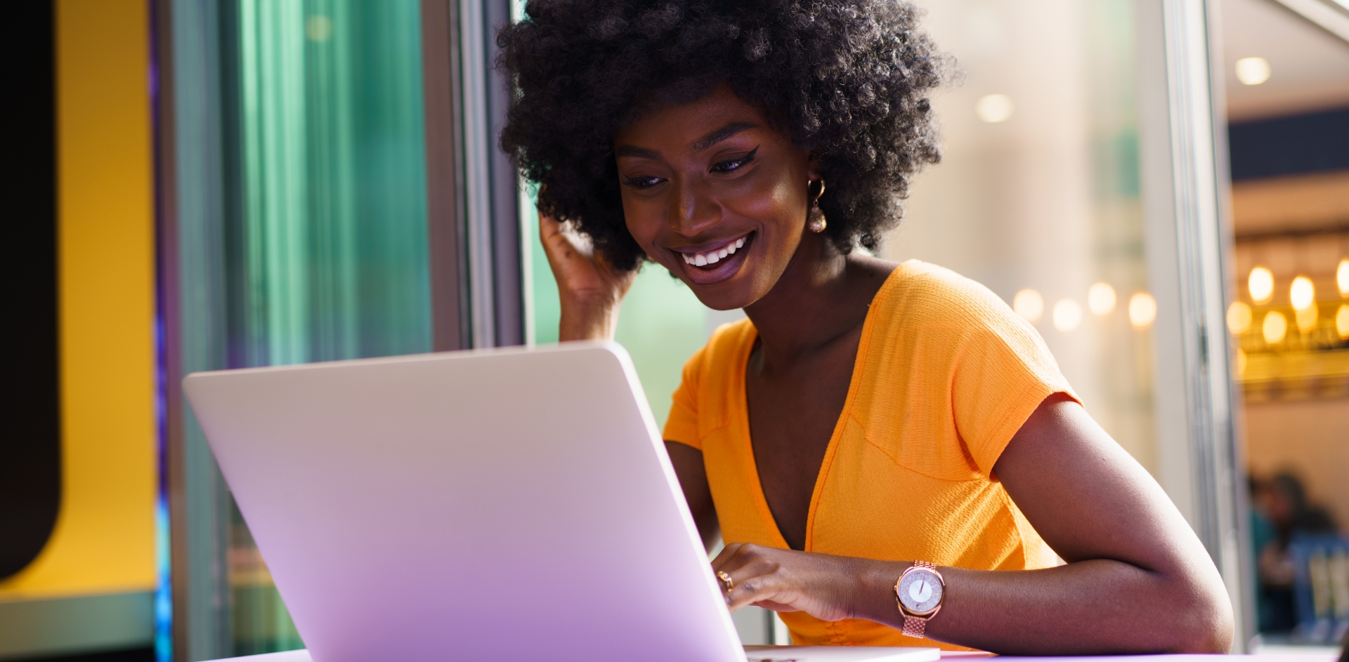 A woman seated using a laptop and holding a cell phone to her ear.