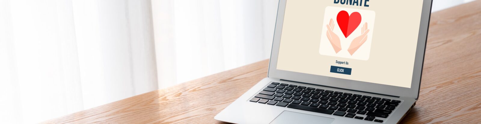 laptop sitting on a wooden desk. laptop screen says "donate" with a picture of a heart.