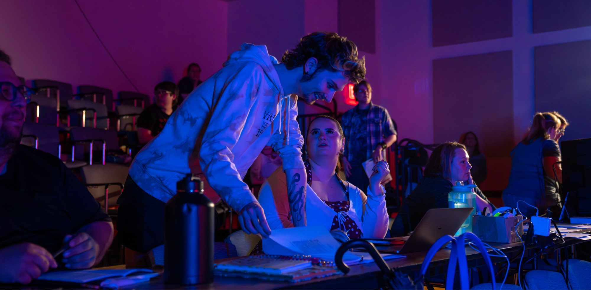 People talking while others are seated in rows of auditorium seats behind them.