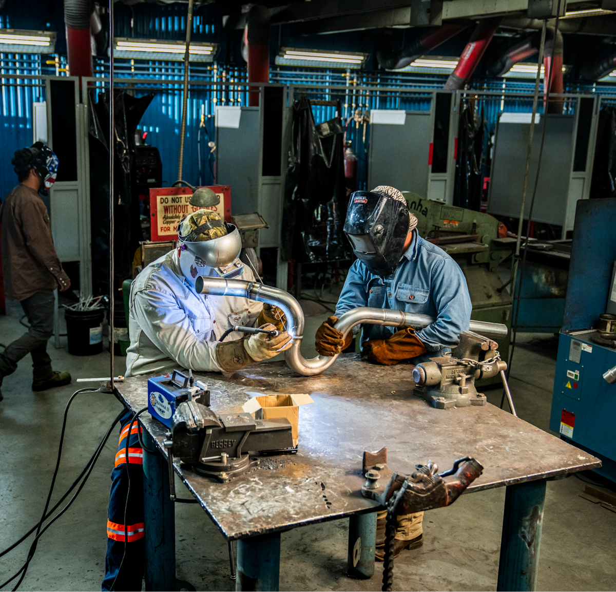 Two people wearing welding gear working on a tailpipe.