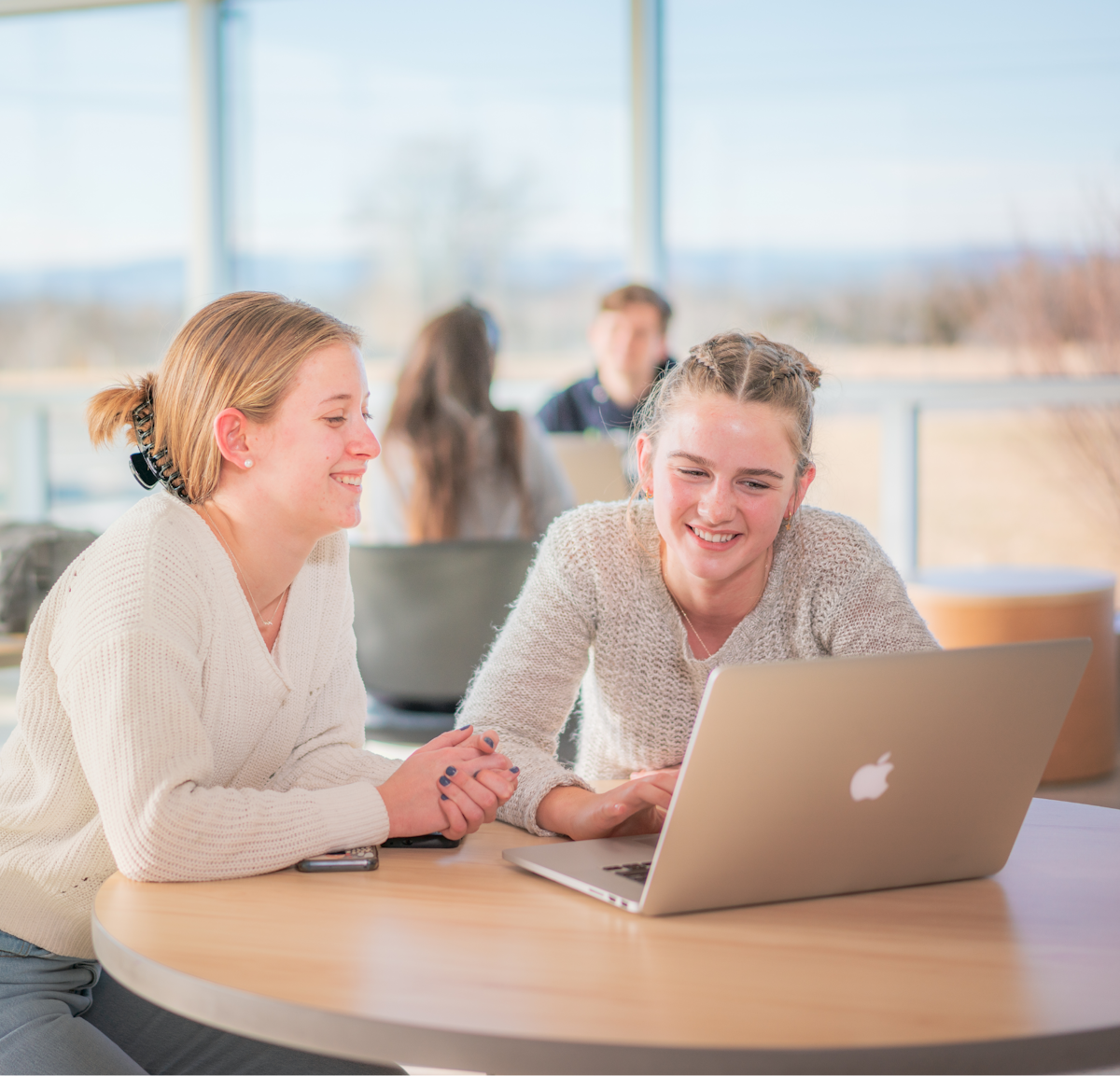 Two women seated at a round table looking at a laptop