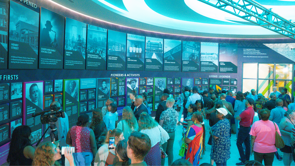 A large group of people standing in front of a wall depicting pictures and information about local historical figures.