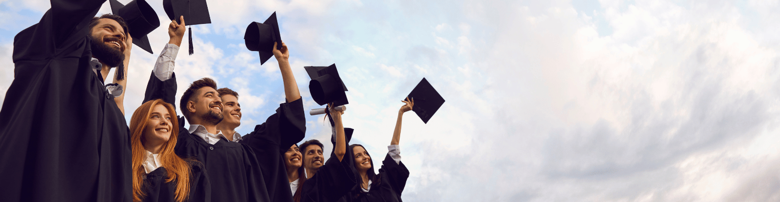 Students in black graduation robes holding black mortarboards, with some hats thrown in air.
