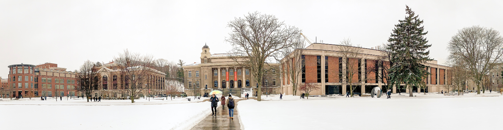 Photo shows college campus building covered in snow, with students walking along a pathway.